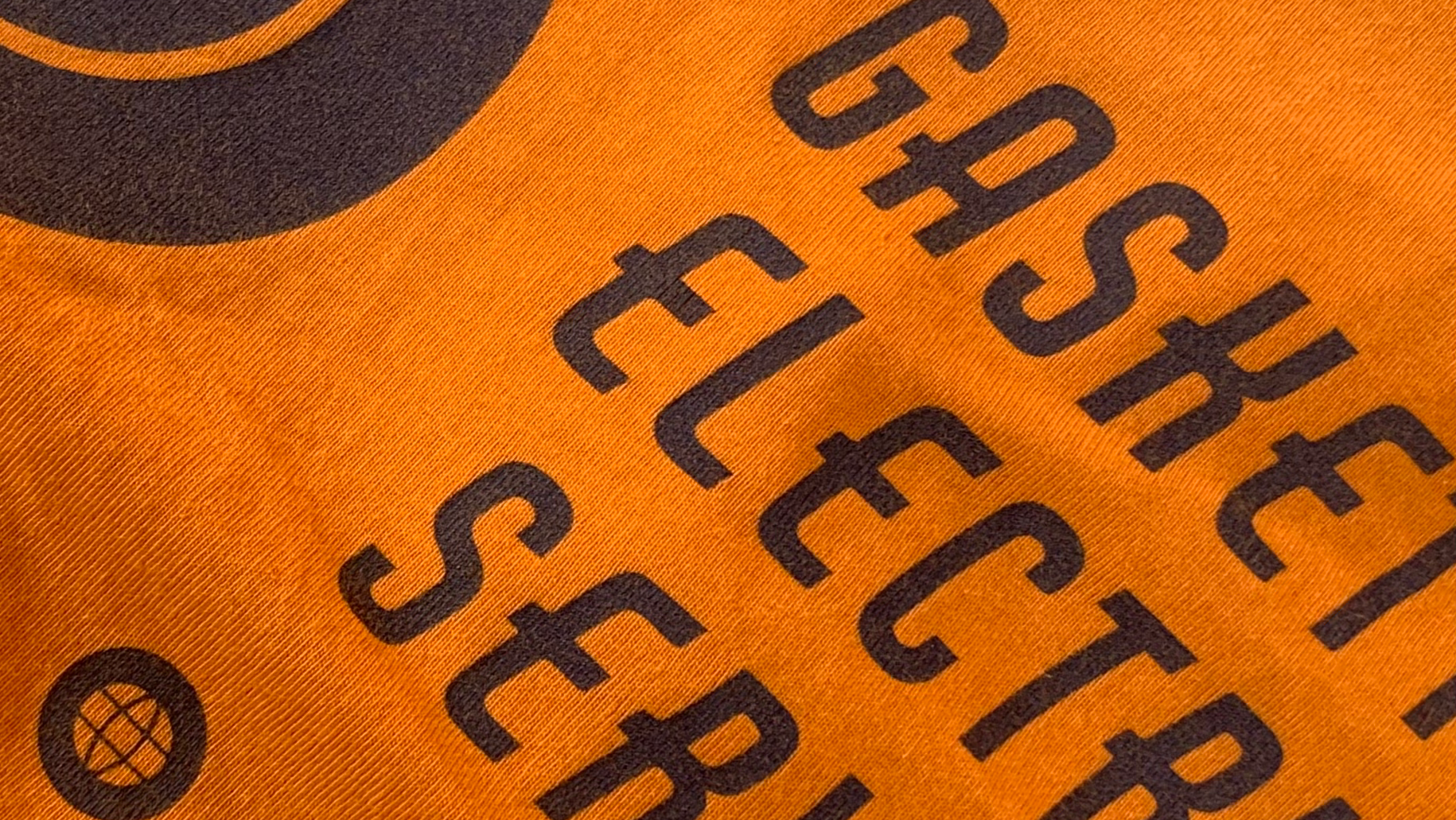Close up of the Gaskett Electrical Services work shirt, charcoal lettering printed on hi vis orange fabric