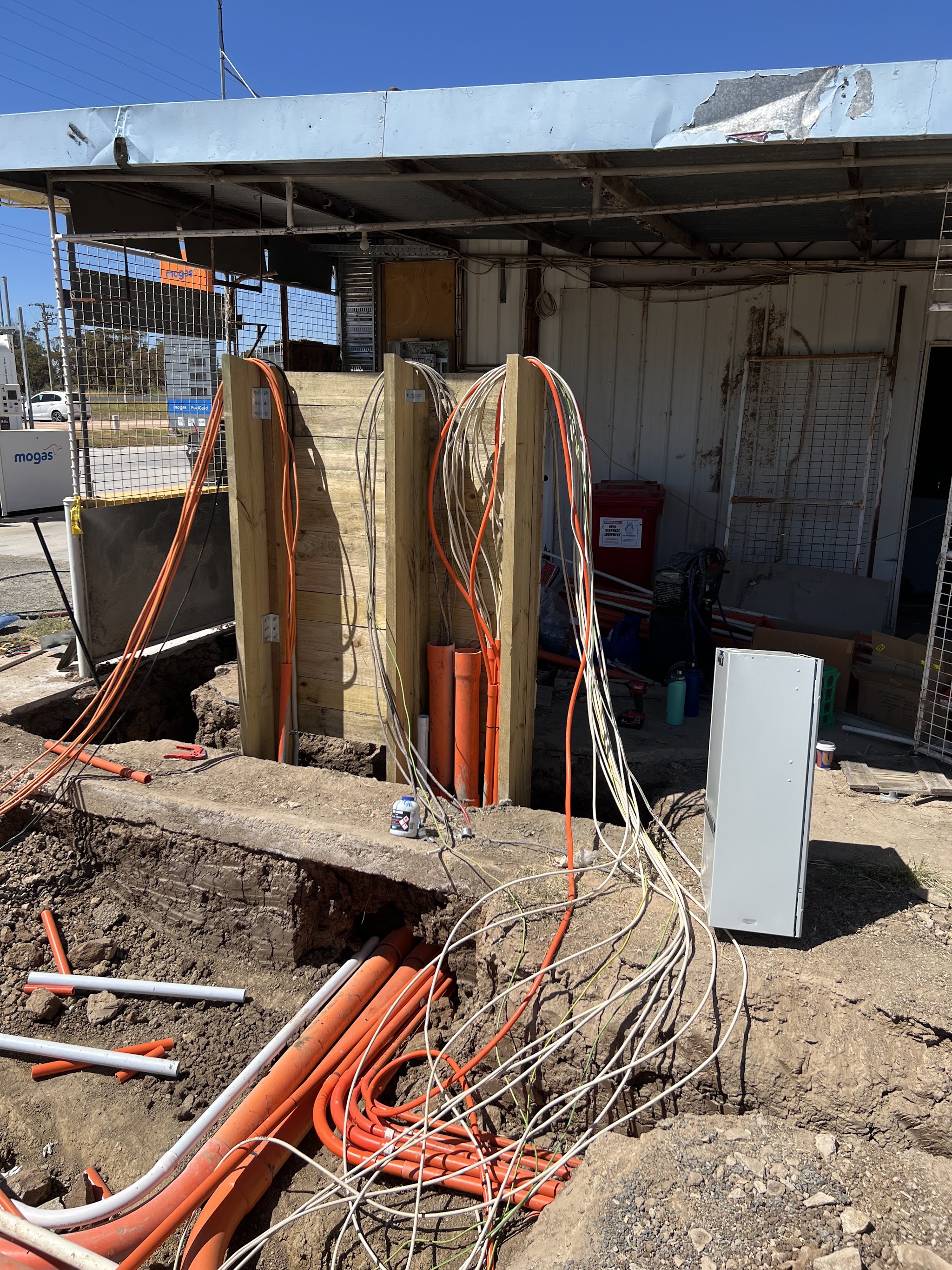 A service station mid rebuild with banks of orange conduit, a new outdoor switchboard cabinet and multi core cable runs
